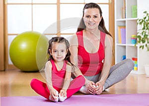 Young mother with little daughter exercising in gym at home