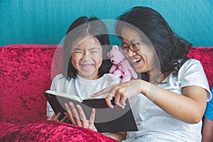 Young mother and little daughter girl reading a book on sofa at