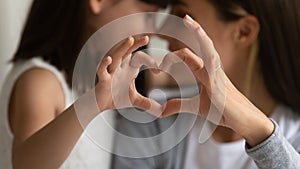 Young mother and little daughter posing making heart gesture