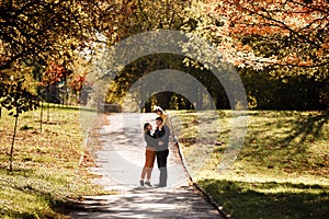 Young mother and little daughter sitting on fathers shoulders are walking outdoors at autumn park. Dad, mom and child