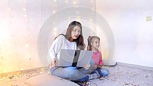 Young mother with little daughter sitting floor doing shopping at online store.