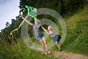 A young mother and a little girl are running along the path with a kite. Summer day, wildflowers