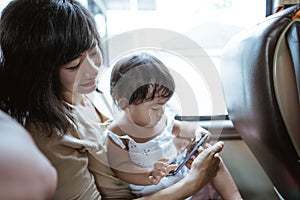 a young mother and little girl see a video on their cellphone sitting on the bus