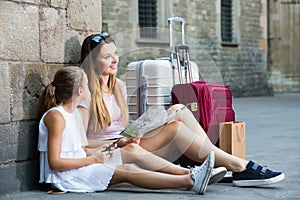 Young mother with little girl travelling together relaxing near old building using map and phone