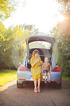 Young mother and little son travelers sit in trunk of car on road and blow soap bubbles. Photo about family travel