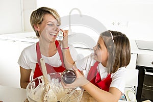 Young mother and little sweet daughter in cook apron cooking together baking at home kitchen