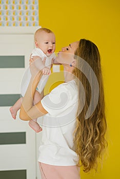 Young mother with long hair holds a baby in her arms and kisses him at home