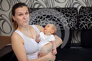 A young mother looks at her newborn baby in surprise. Woman holds a baby