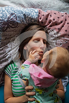 Young mother lying on the bed with her baby daughter lying on top of her