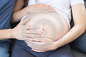 A young mother is making a heart-shaped hand on her stomach. Happy pregnant asian woman with heartshaped by hand in sofa bed