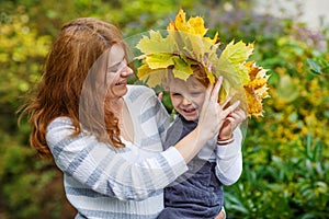 Young mother in a maple leaf wreath holding little toddler boy