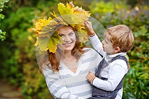 Young mother in a maple leaf wreath holding little toddler boy