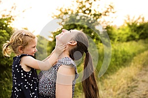 Young mother in nature holding little daughter in the arms.