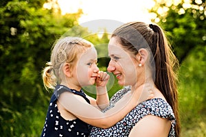 Young mother in nature holding little daughter in the arms.