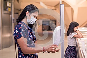 Young mother on new normal using the alcohol antiseptic gel. Washing hands using sanitizer dispenser while her daughter waits on