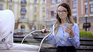 Young mother in office suit working smartphone and smiling to baby in carriage