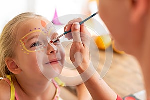 Young mother painting daughters face for Halloween party. Halloween or carnival family lifestyle background. Face painting.