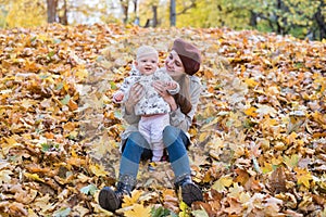 Young mother playing with baby in autumn Park. Mother and baby sitting on fallen leaves
