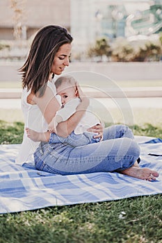 young mother playing breast feeding her baby girl outdoors in a park, happy family concept. love mother daughter