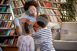 A young mother playing a guitar to her little children at home. Family, home, playtime