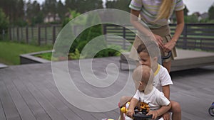 Young mother playing and having fun with her baby boy son brothers in a green garden with cars - family values warm