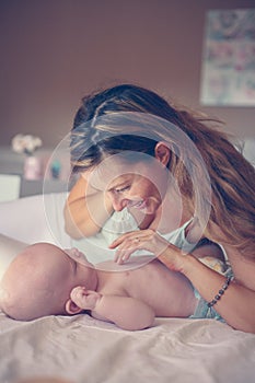 Young mother playing with her baby boy in bed.