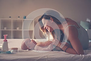 Young mother playing with her baby boy in bed. Mother enjoying i