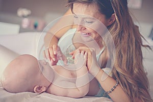 Young mother playing with her baby boy in bed. Mother enjoying i