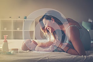 Young mother playing with her baby boy in bed. Mother enjoying i