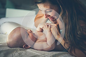 Young mother playing with her baby boy in bed. Mother enjoying i