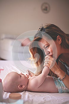 Young mother playing with her baby girl in bed. Mother enjoying