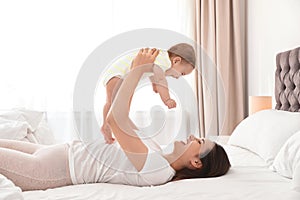 Young mother playing with her cute baby on bed