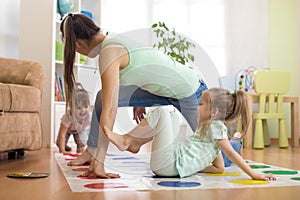 Young mother playing twister with her daughters. Happy family have a fun time in holiday