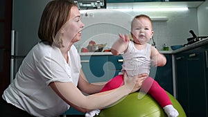 A young mother plays with a child, putting her on a fitball. The concept of sports training with children