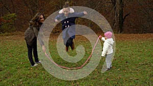 Young mother plays with children in the autumn forest. Little beautiful girl jumping rope. The family is happy.