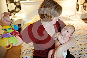 Young mother plays with her baby rattles in evening at home photo