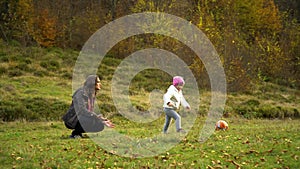 A young mother plays with her little daughter in the autumn forest. Mom with a little beautiful girl playing ball.