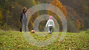 A young mother plays with her little daughter in the autumn forest. Mom with a little beautiful girl playing ball.