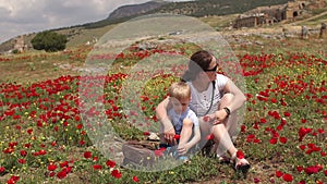 A young mother plays with her little son in a field with flowering poppies.