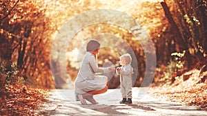 Young mother plays with her son in the autumn forest. Blond in a sports gray suit. Autumn leaves. Joyful family in