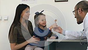 Young mother proud of her little girl and doctor giving her a lollipop after the exam