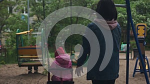 Young mother pushes daughter on a swing. Little girl on the playground.