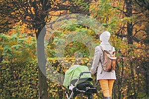 Young mother pushing stroller in autumn park