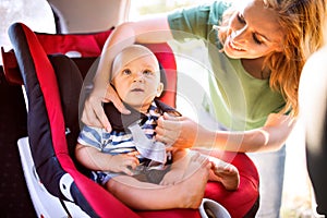 Young mother putting baby boy in the car seat.