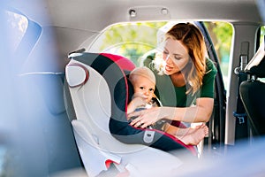 Young mother putting baby boy in the car seat.