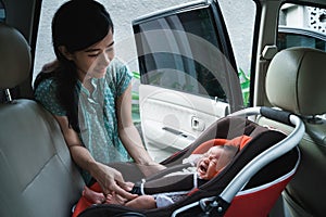 Young mother putting her daughter in car seat