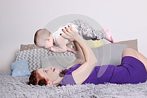 Young mother raises her little baby on bed