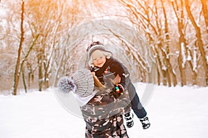 Young mother raising up her baby son outdoors in winter park. Happy winter holidays. Family on a winter walk. Winter fashion,