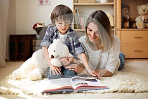 Young mother, read a book to her child, boy in the living room o