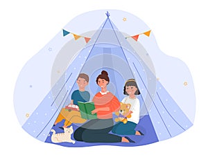 Young mother is reading book and telling story for little son and daughter in the teepee tent